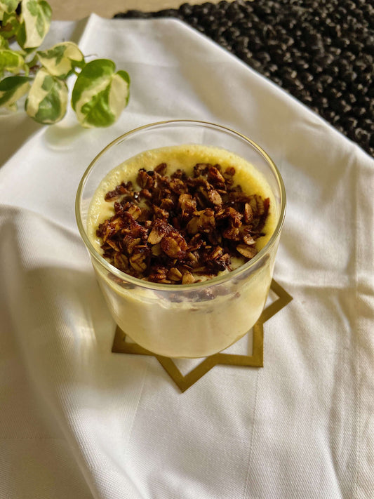 yellow pineapple turmeric smoothie glass topped with chocolate granola on a white background