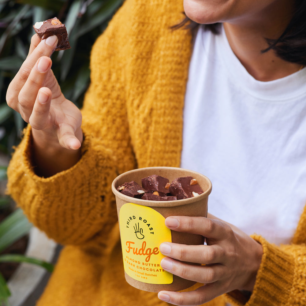a woman in a yellow sweater eating a delectable fudge brownie from a brown paper tub