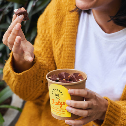 a woman in a yellow sweater eating a delectable fudge brownie from a brown paper tub 