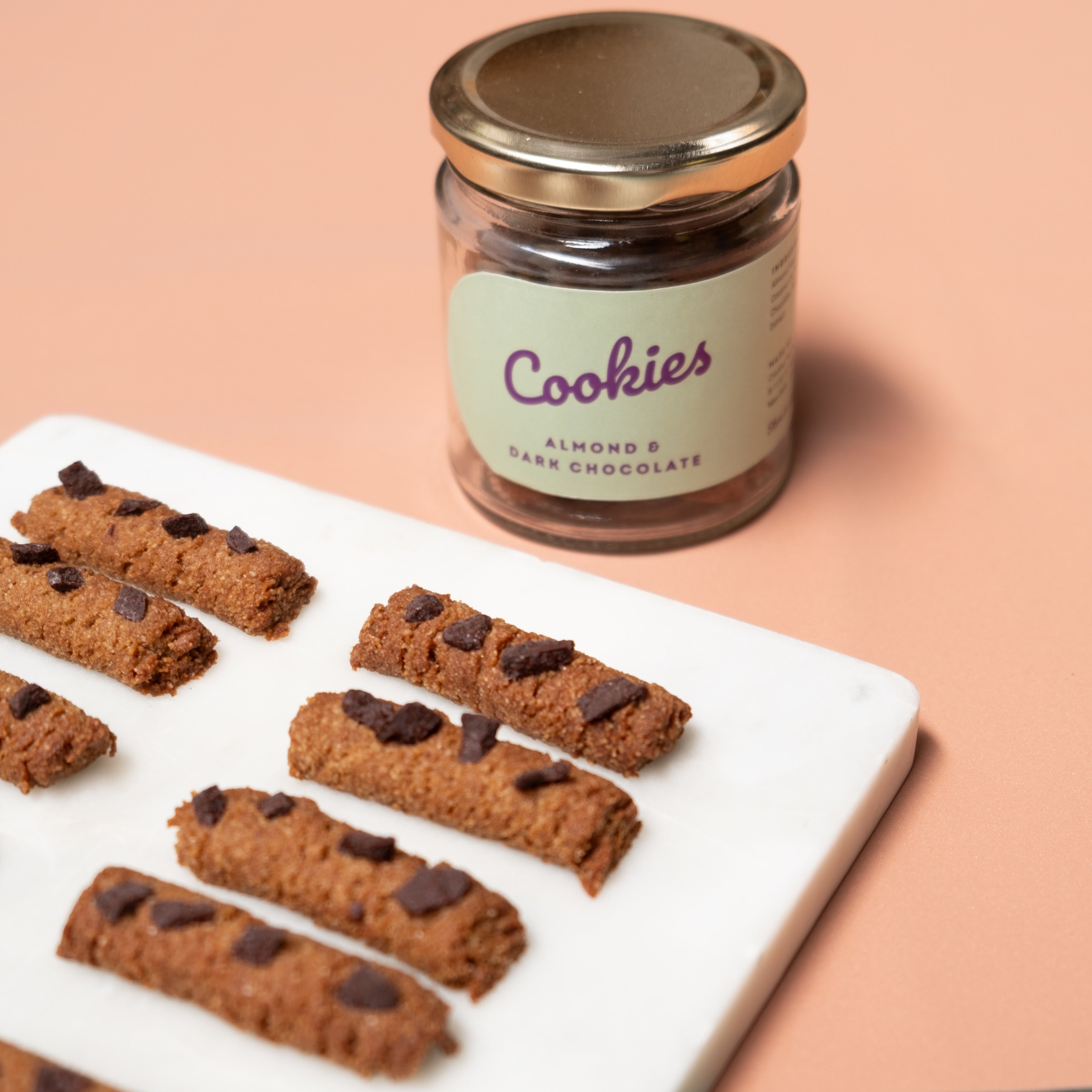 cookie sticks displayed on a white marble tray with a glass jar on an orange background